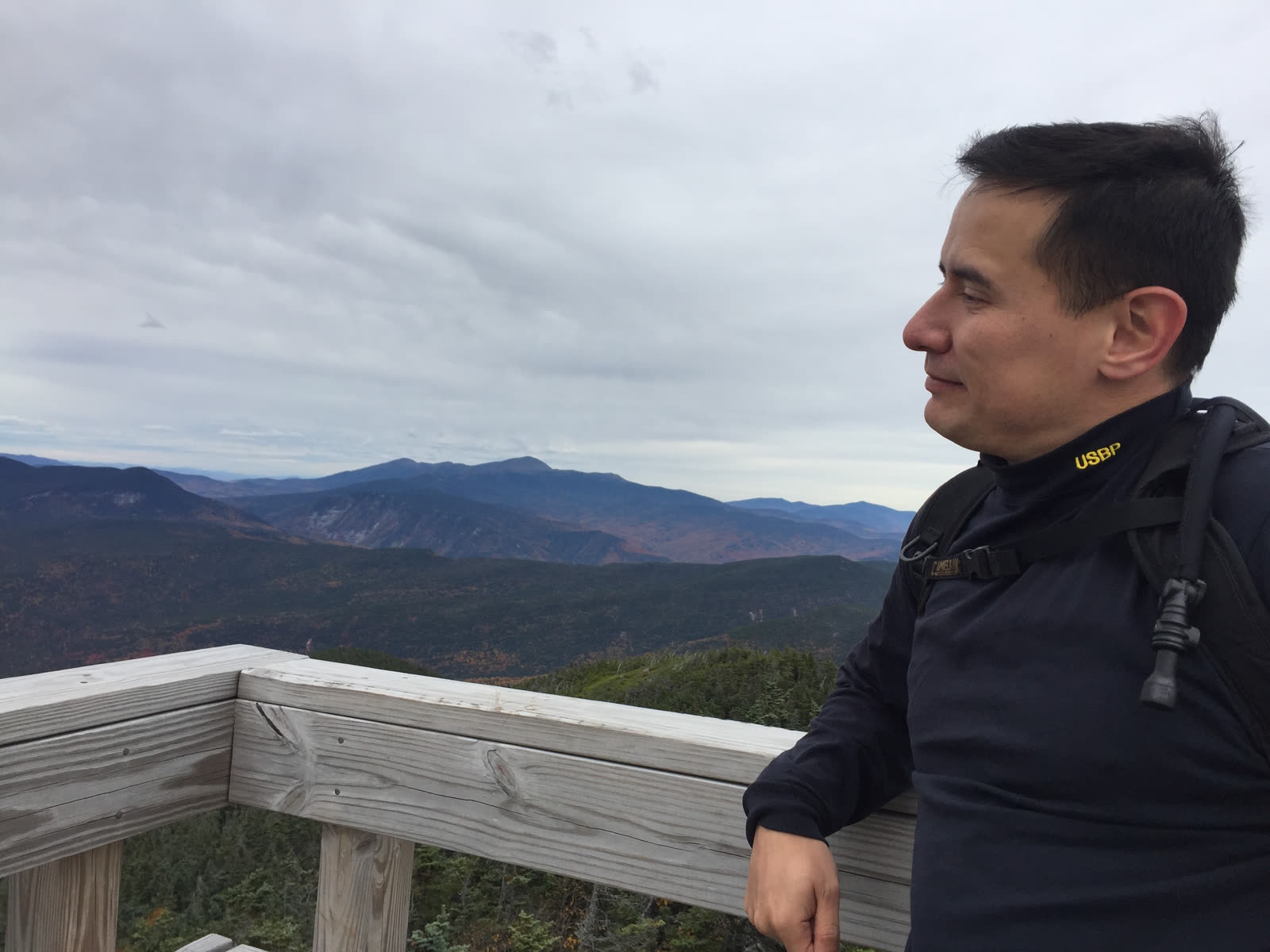F. Joseph Blecha II in profile on a wooden overlook, mountains behind.